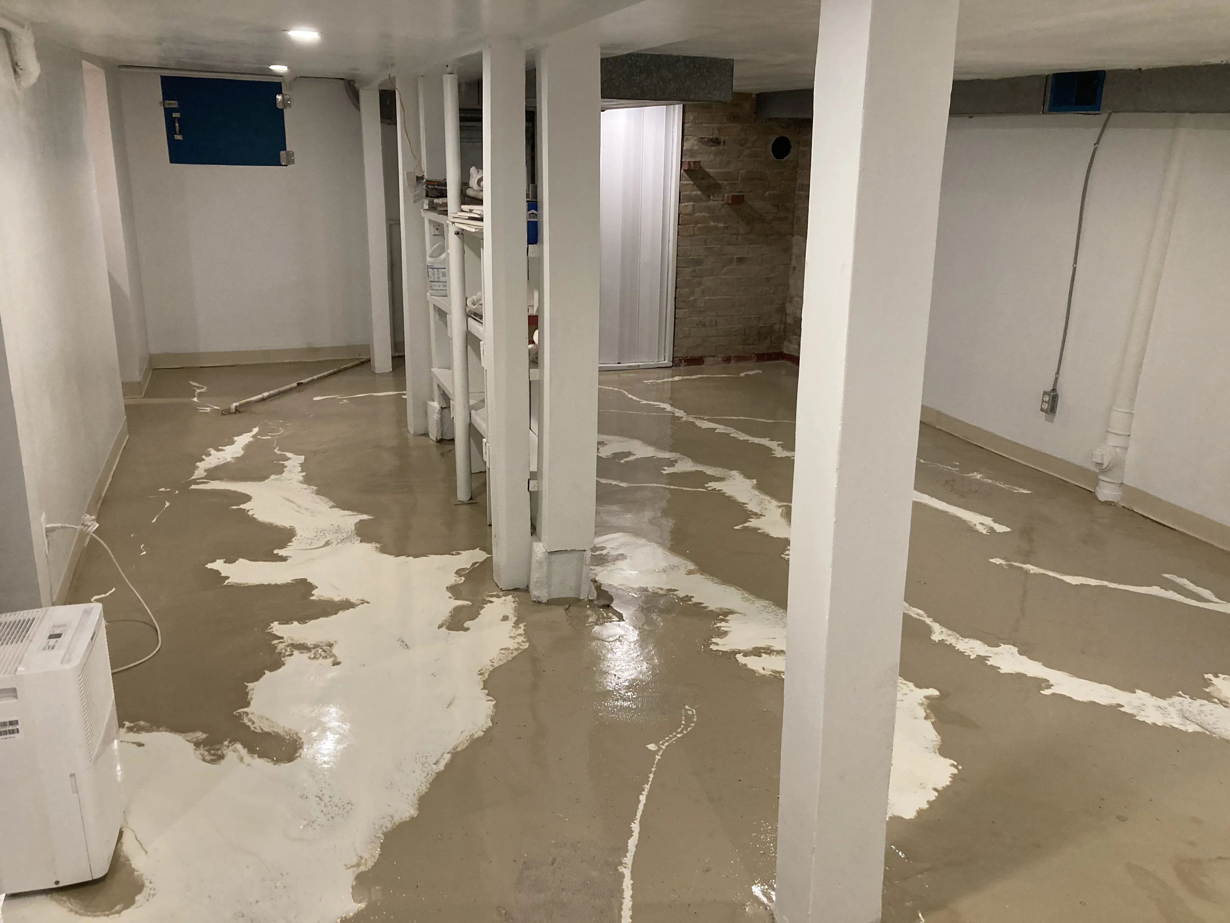 Basement concrete floor with white epoxy coating and support columns during preparation phase