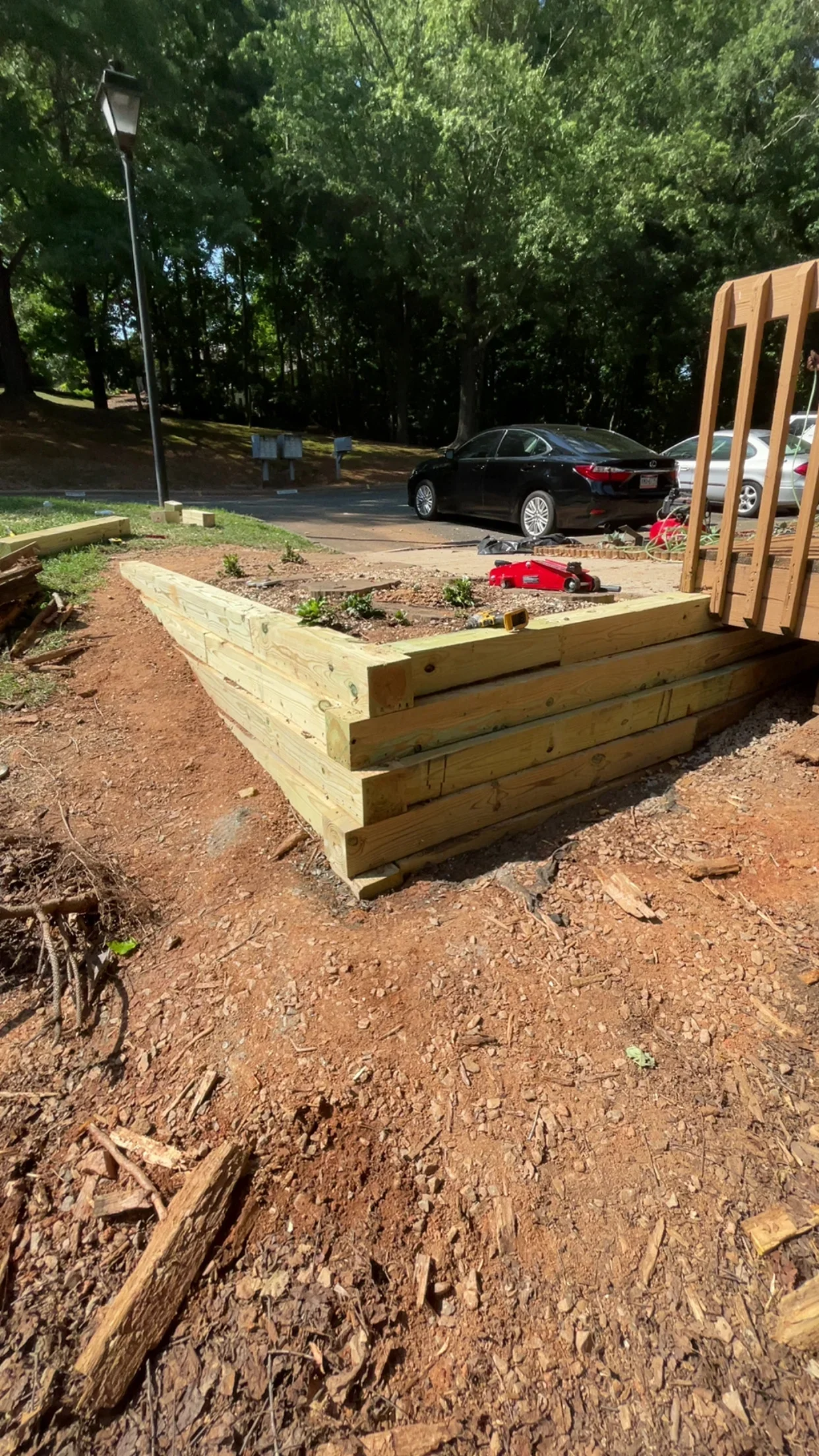 Tiered pressure-treated wood raised garden bed with soil and plantings in landscaped yard