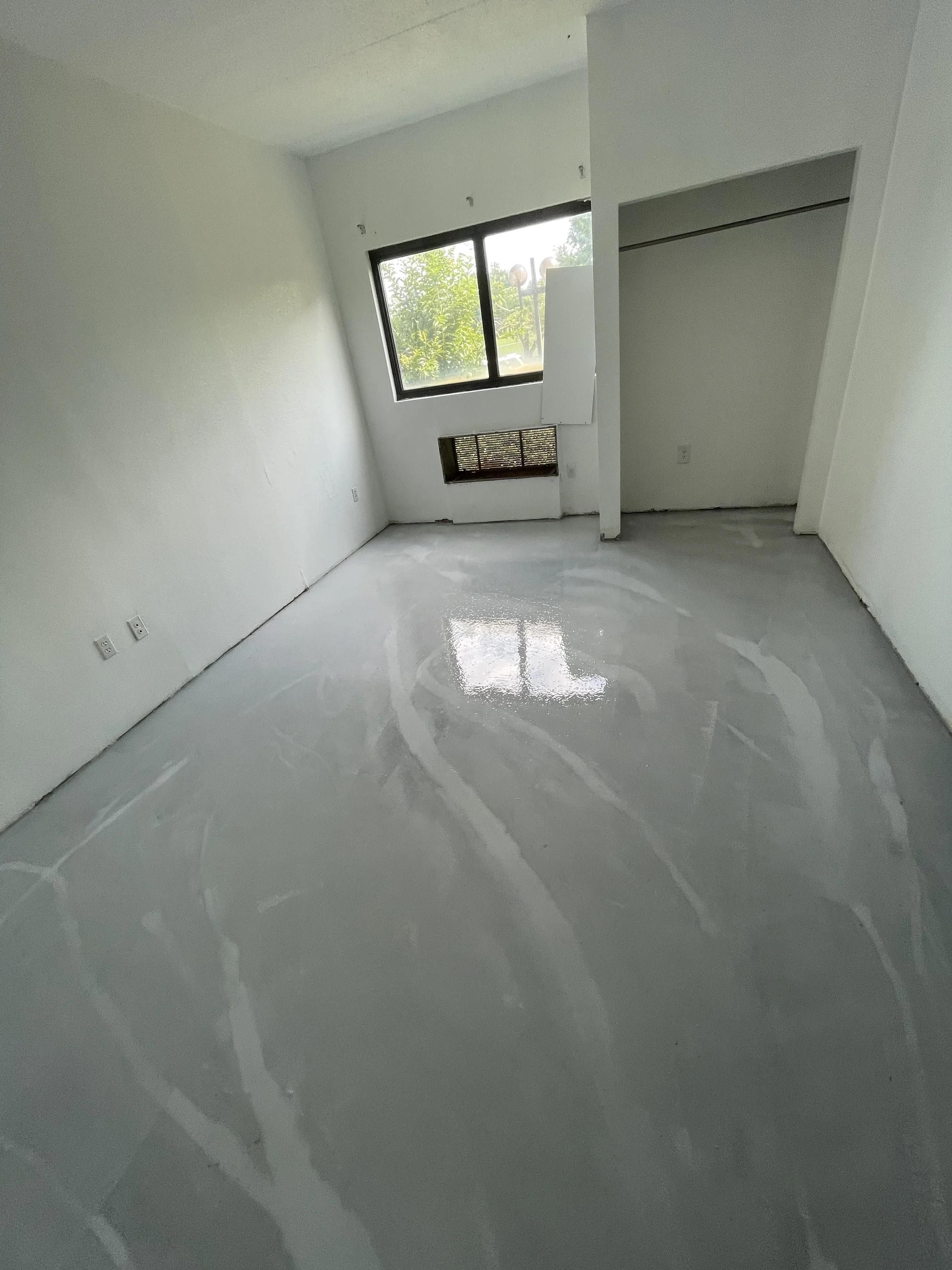Interior room with white drywall, black-framed window, and prepared concrete floor