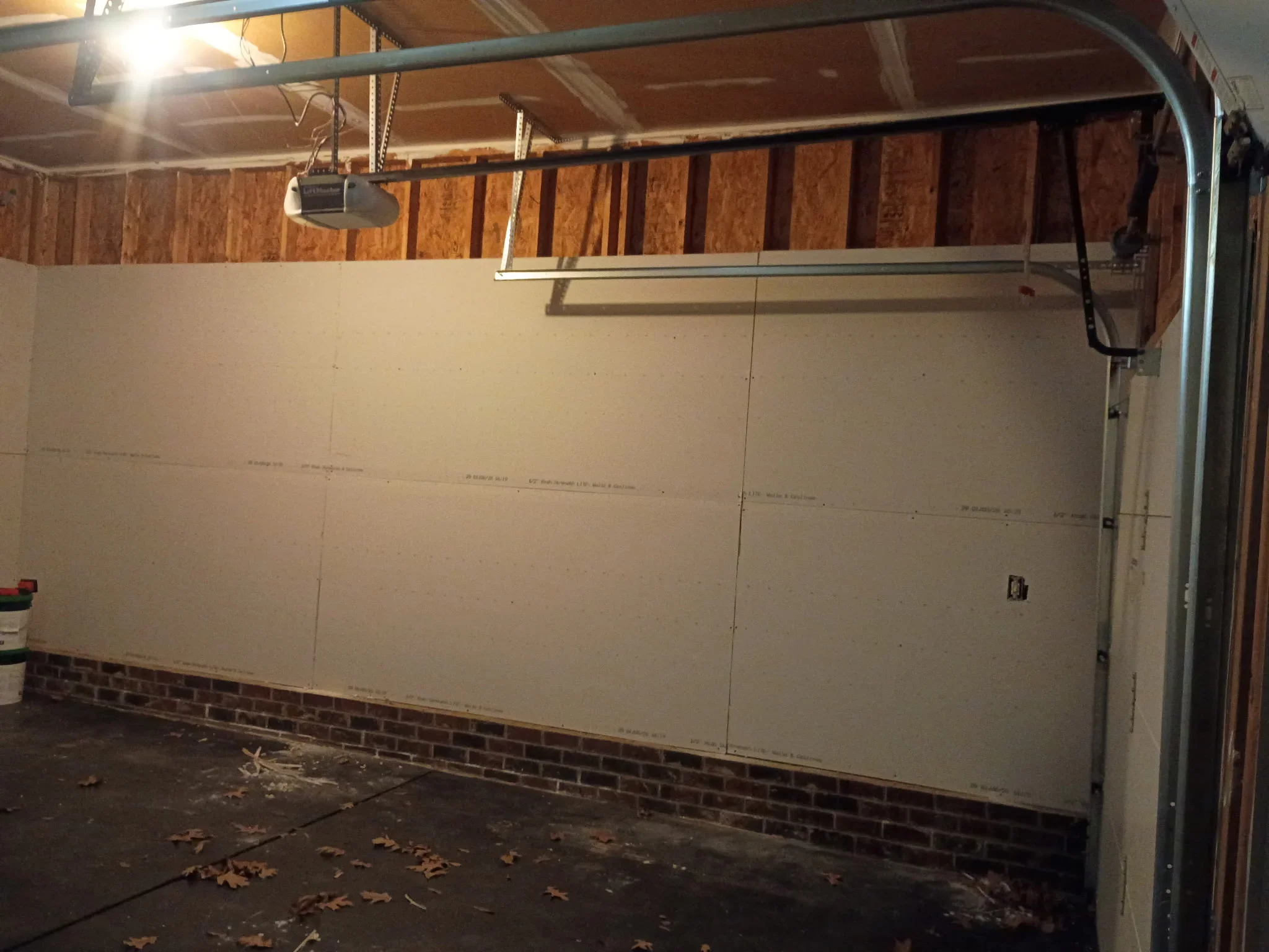 Drywall sheets installed on garage walls with exposed framing and brick foundation