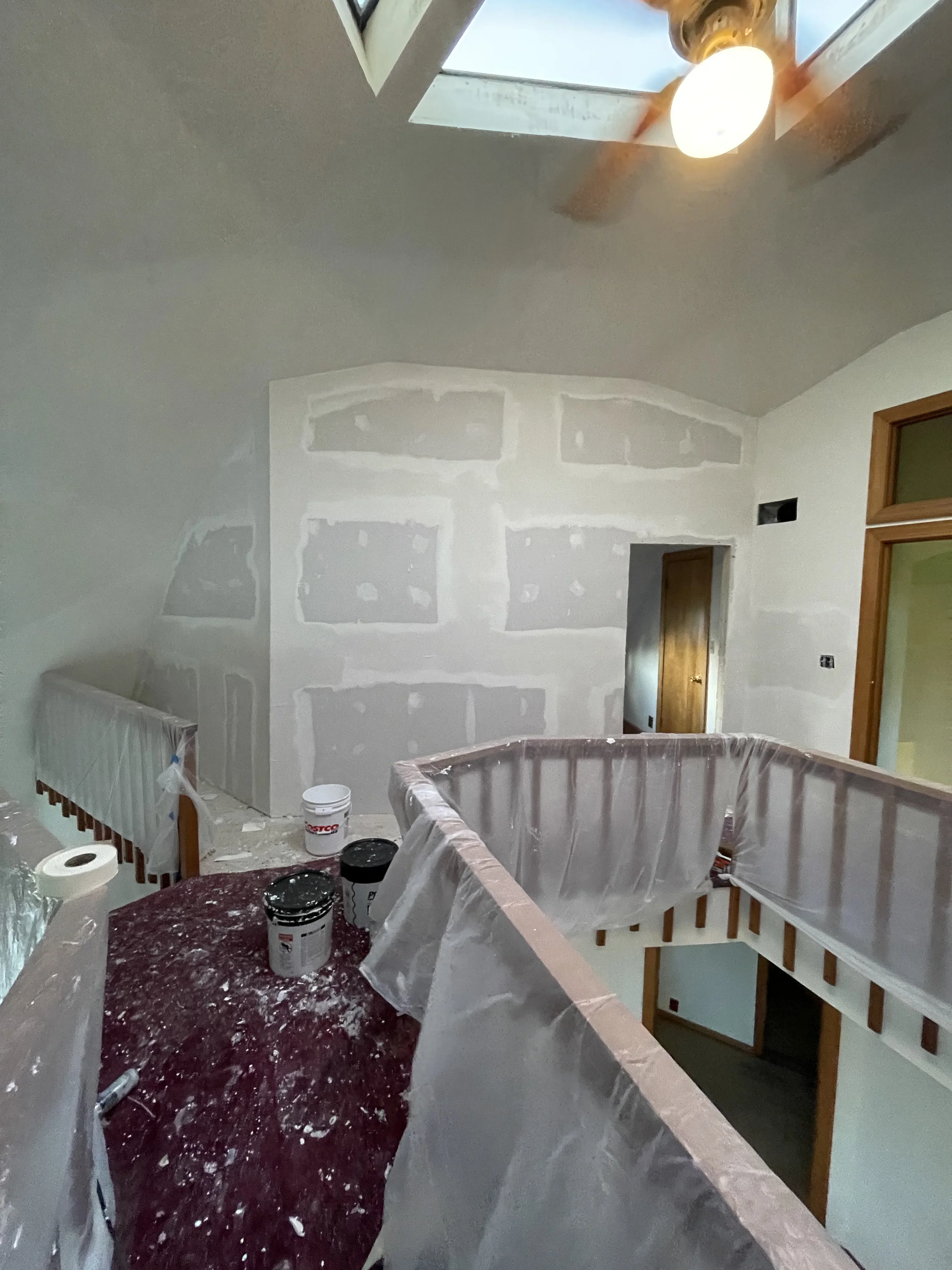 Drywall installation with protective coverings, skylights, and recessed lighting in multi-room interior space