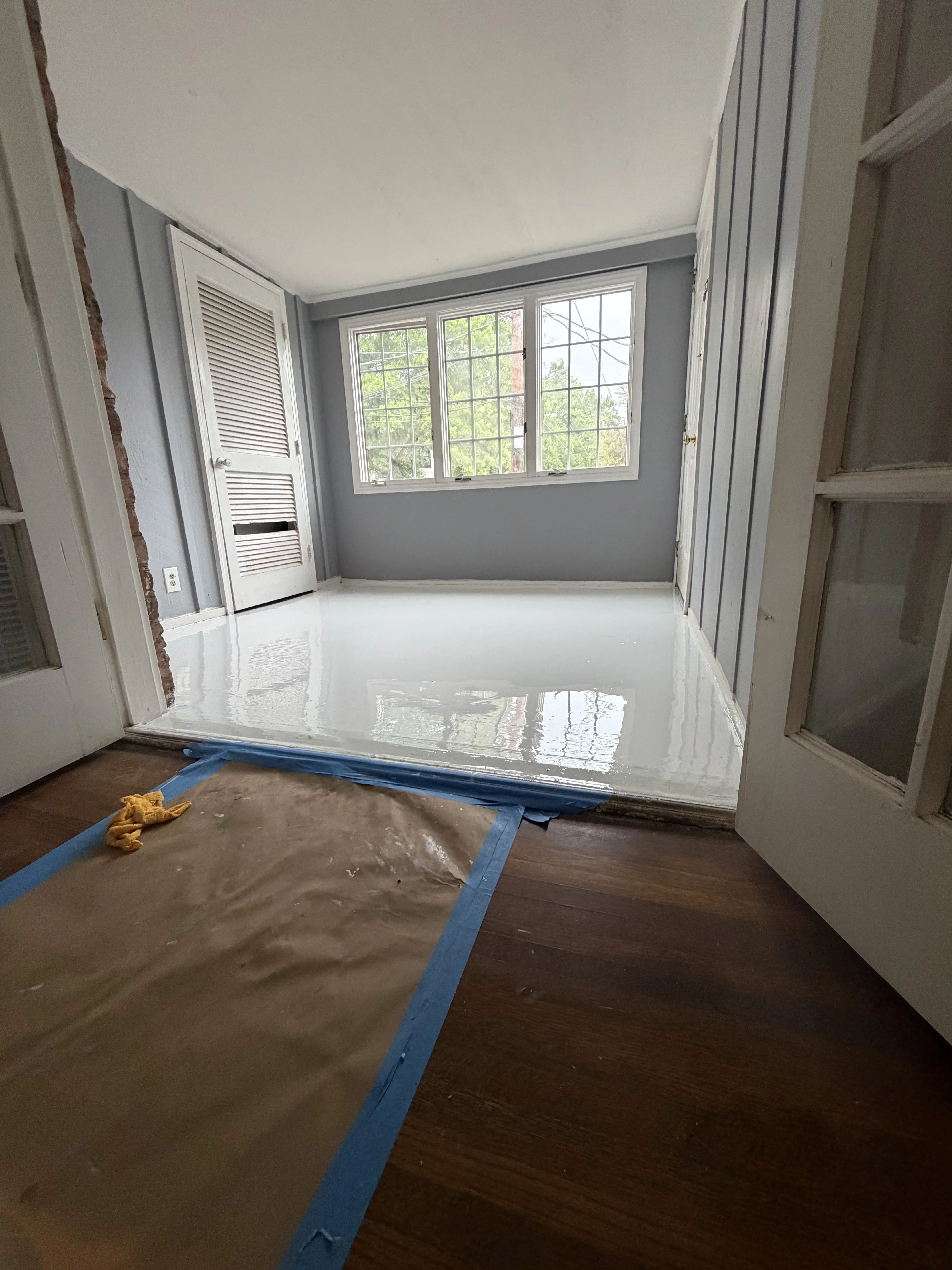 Bright room with white epoxy floor, gray walls, and large windows during renovation