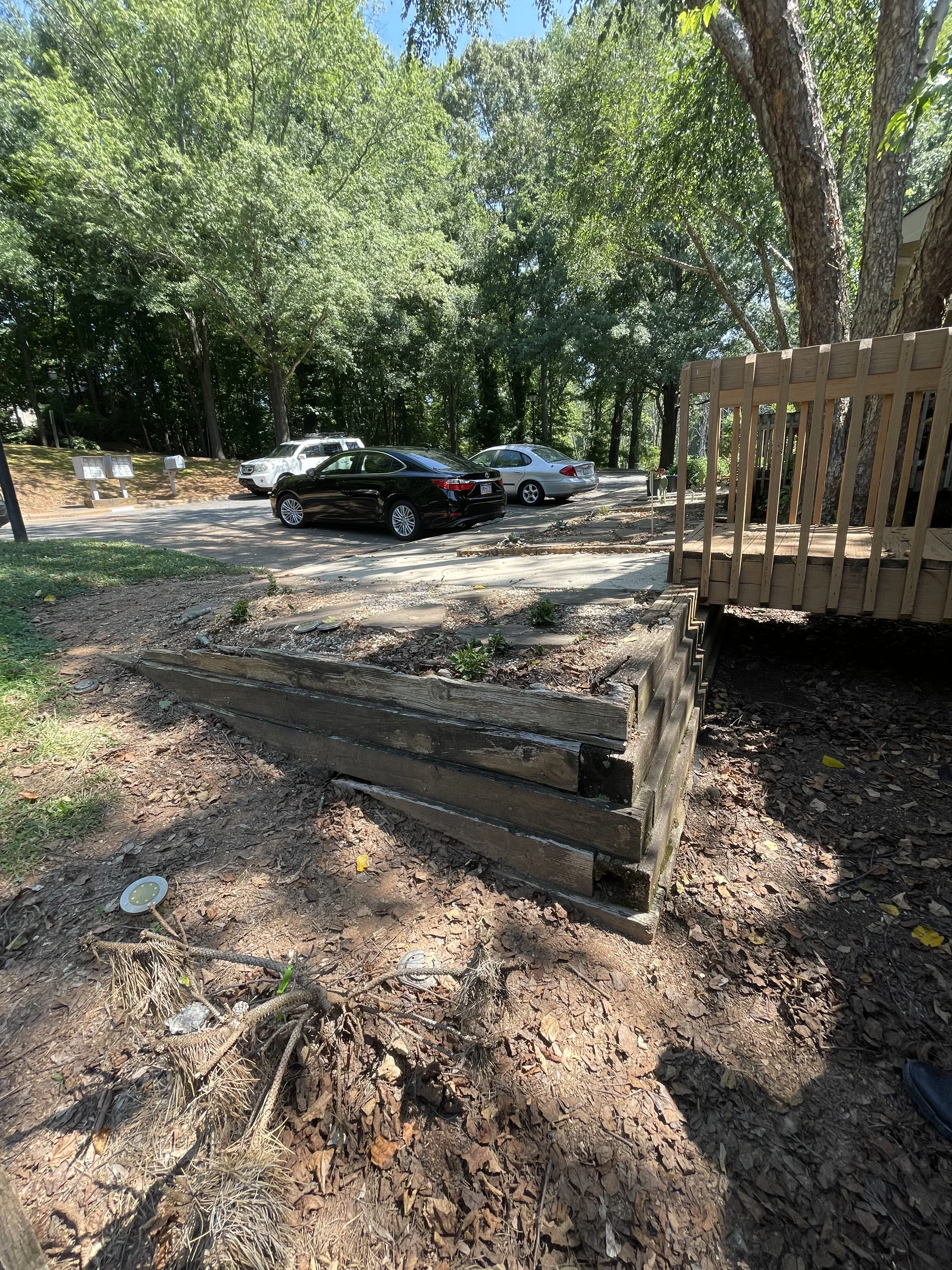 Timber retaining wall, gravel parking area, and landscape grading with mature trees