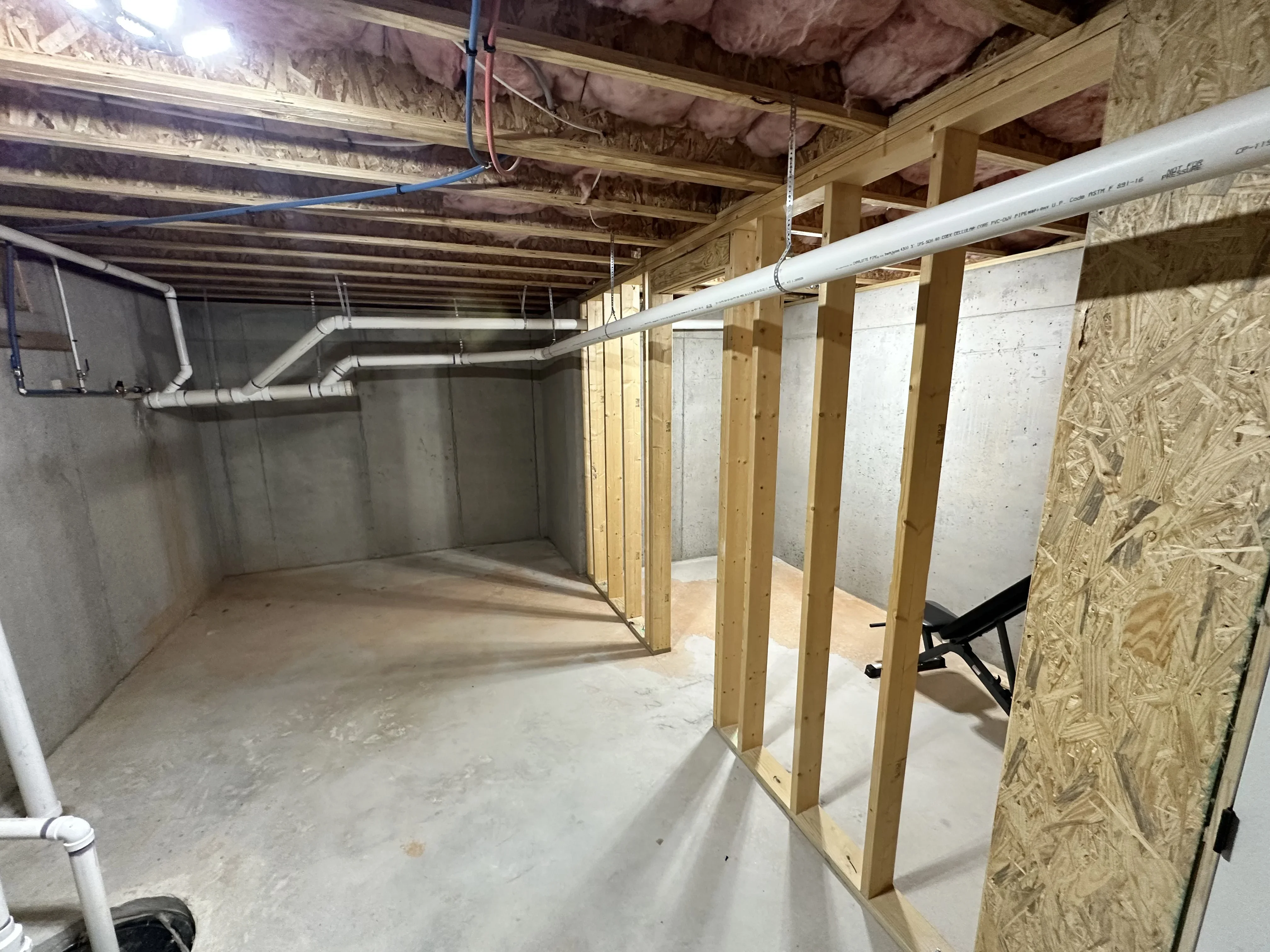 Basement framing with lumber studs, OSB sheathing, concrete walls, and HVAC ductwork installation