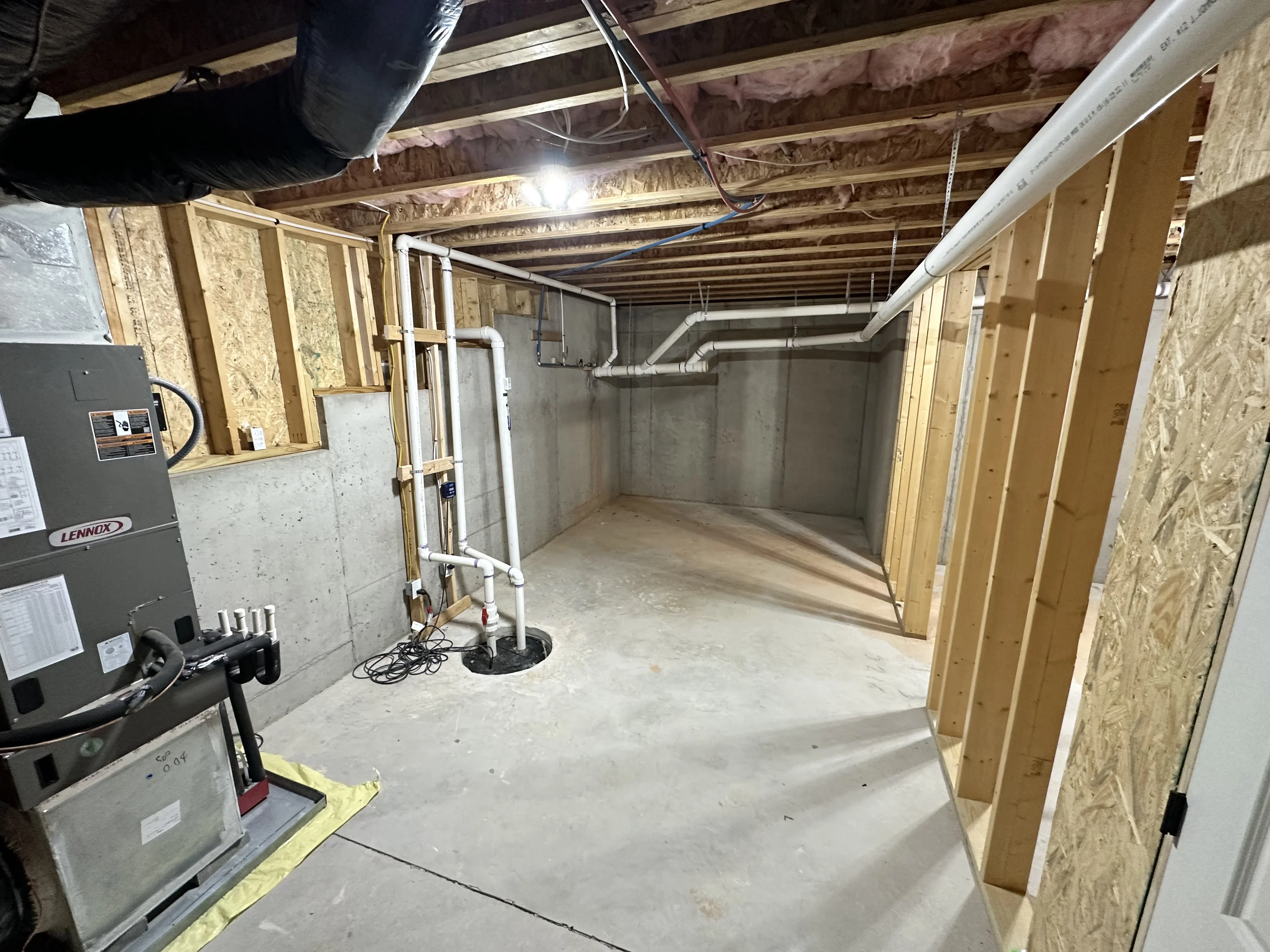 Basement framing with wood studs, concrete foundation, HVAC ducts, and mechanical systems